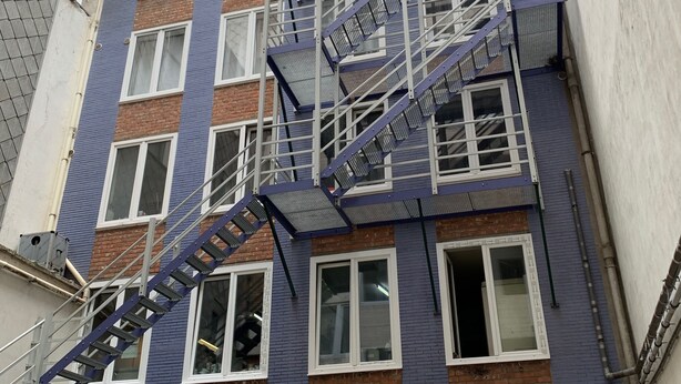 A multi-story building with a fire escape, closed garage doors, and a brick facade. - Apartment Backhouse (Ostend)