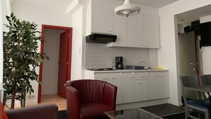 A modern kitchen with white cabinets, a black range hood, and a coffee maker. There is a red chair and a glass table in the living area. - Apartment Backhouse (Ostend)