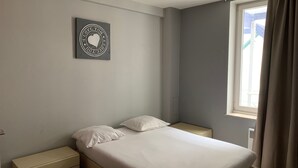 A bedroom with a bed, two bedside tables, a wall-mounted artwork, and a window with curtains. - Apartment Backhouse (Ostend)