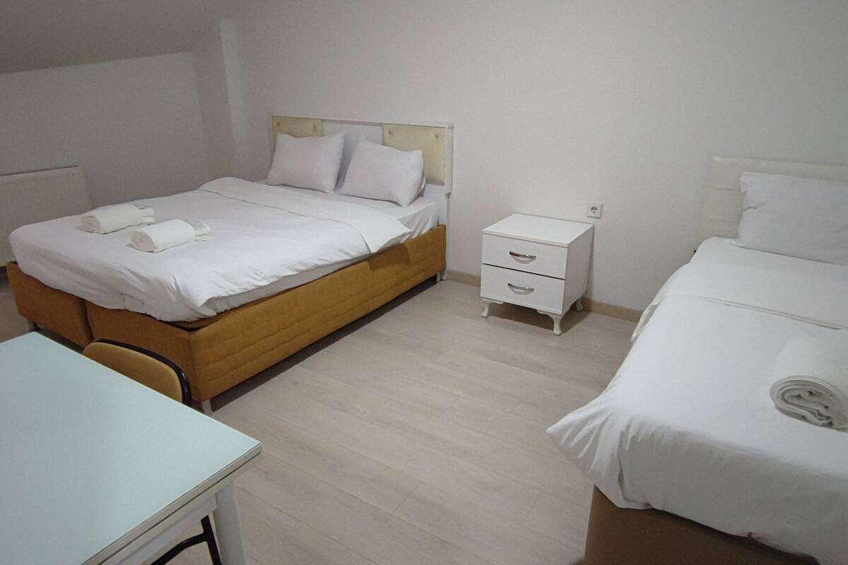 A hotel room with two beds, a small table, and a bedside table with drawers.