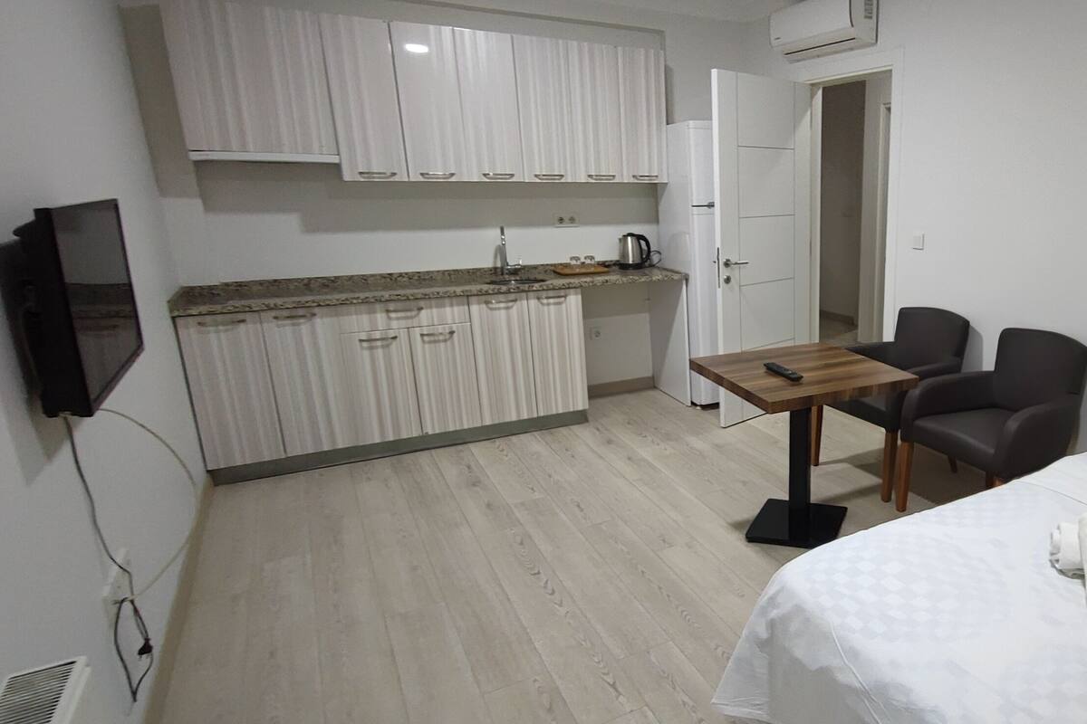A hotel room with a bed, a small table, a chair, a TV, and a kitchenette.