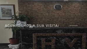 Un comptoir d’accueil surmonté d’une horloge, avec des plantes en pot de chaque côté et une œuvre d’art encadrée accrochée au mur.