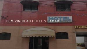 Un hôtel appelé « BEM VINDO AO HOTEL VILAMAR » avec un panneau indiquant « ESTACIONAMENTO » (parking).