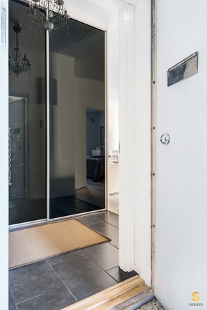 Entrada a una habitación de hotel con puerta de vidrio corrediza, candelabro, un tapete pequeño y suelo de madera.