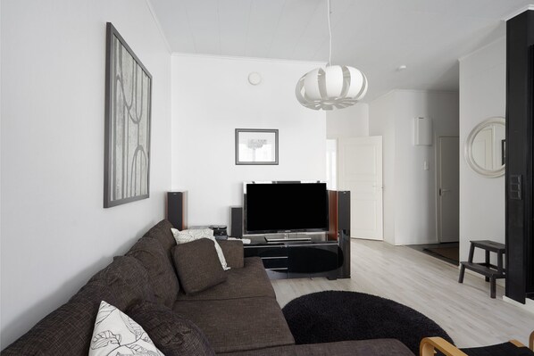 A modern living room with a sofa, TV, speakers, and artwork on the walls.