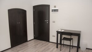 Una habitación con dos puertas de madera oscura, una mesa pequeña con una silla y un cubo de basura.