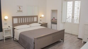 Un dormitorio con una cama de madera, mesitas de noche, un tocador, un aparador, un espejo y una ventana con vistas.