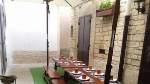 Un comedor con largas mesas y bancos de madera, suelo verde y pared de piedra.