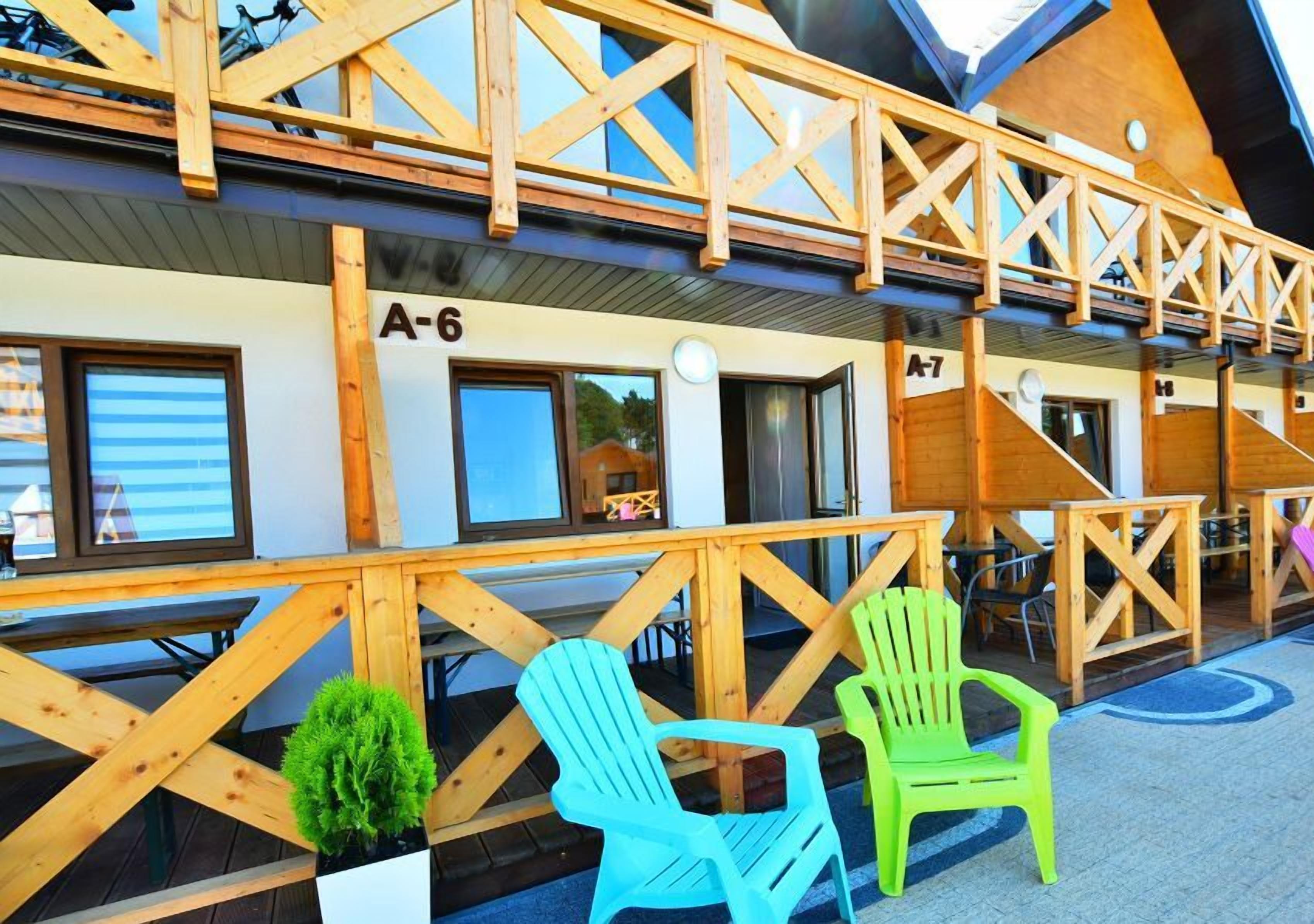 A wooden building with balconies, numbered rooms A-6 and A-7, and outdoor seating with chairs.