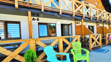 A wooden building with balconies, numbered rooms A-6 and A-7, and outdoor seating with chairs.