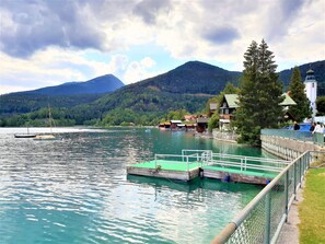 Blick auf einen See mit Booten, einem Steg und Häusern im Hintergrund.