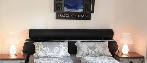 Una cama doble con cabecera oscura, dos mesitas de noche con lámparas y una obra de arte enmarcada sobre la cama.