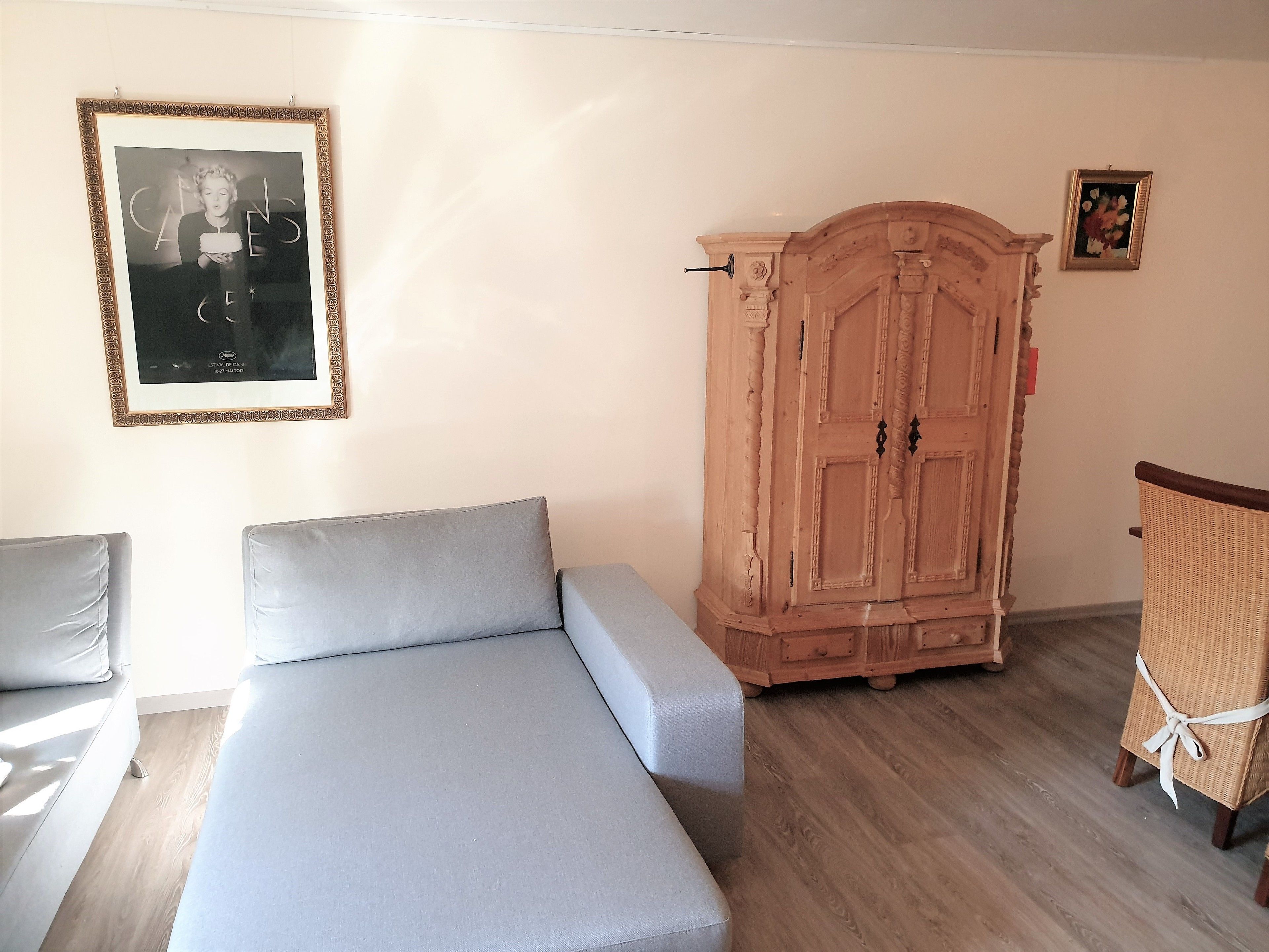 A room with a grey sofa, a wooden cabinet, and a wicker chair.