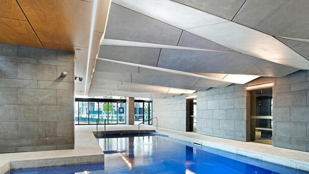 An indoor swimming pool with a clear view of the pool area, a modern ceiling design, and a visible elevator. - Open View towards Stadium - Southern Cross 2B2Bath (Melbourne)