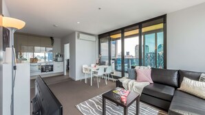A modern apartment with a living room, dining area, and kitchen. It features large windows offering a city view. - Open View towards Stadium - Southern Cross 2B2Bath (Melbourne)