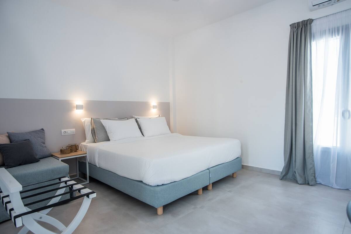 A modern bedroom with a bed, bedside tables, a small sofa, and a window with curtains.