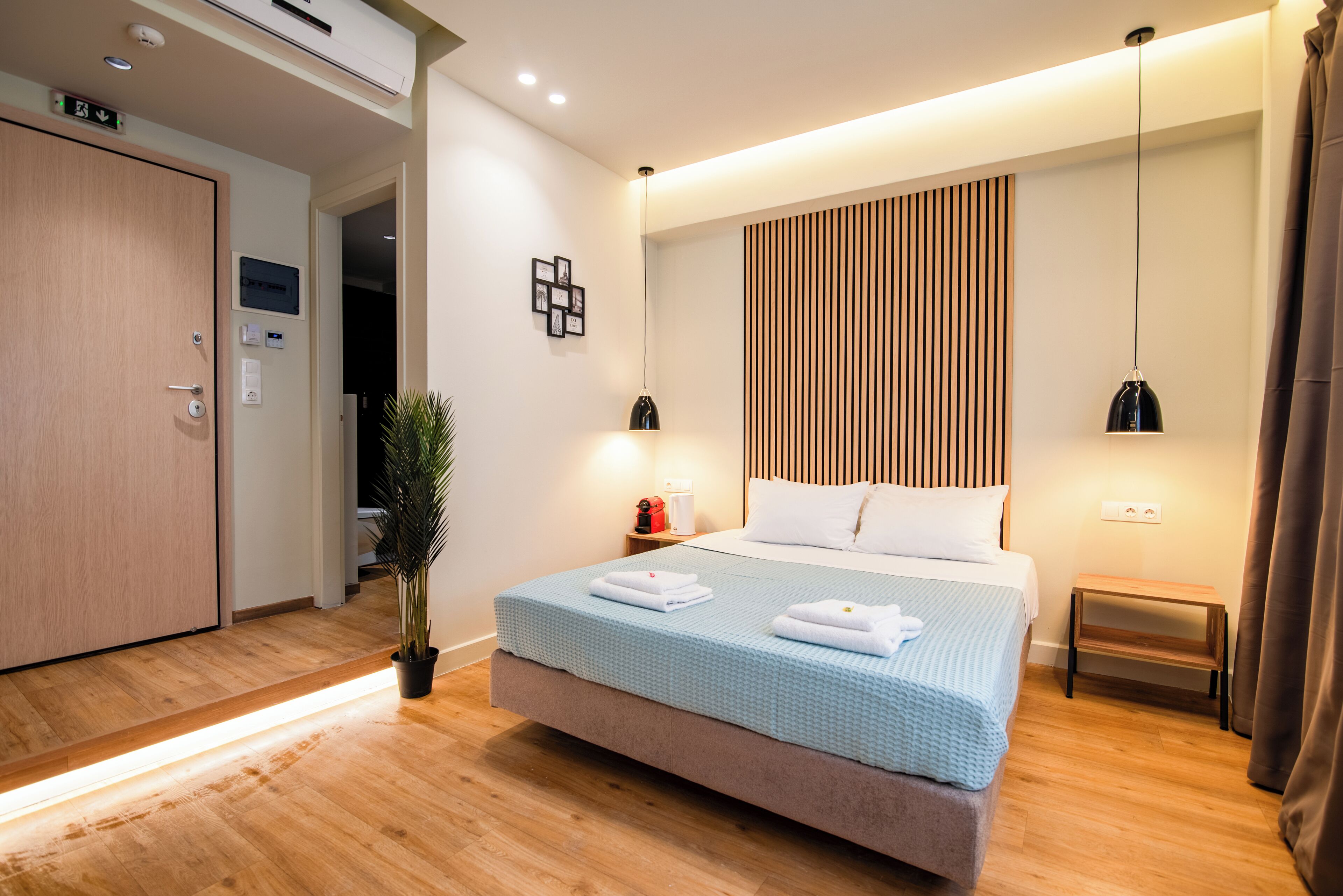 Una habitación de hotel moderna con una cama grande, mesitas de noche, una planta en maceta y un panel de pared de madera.