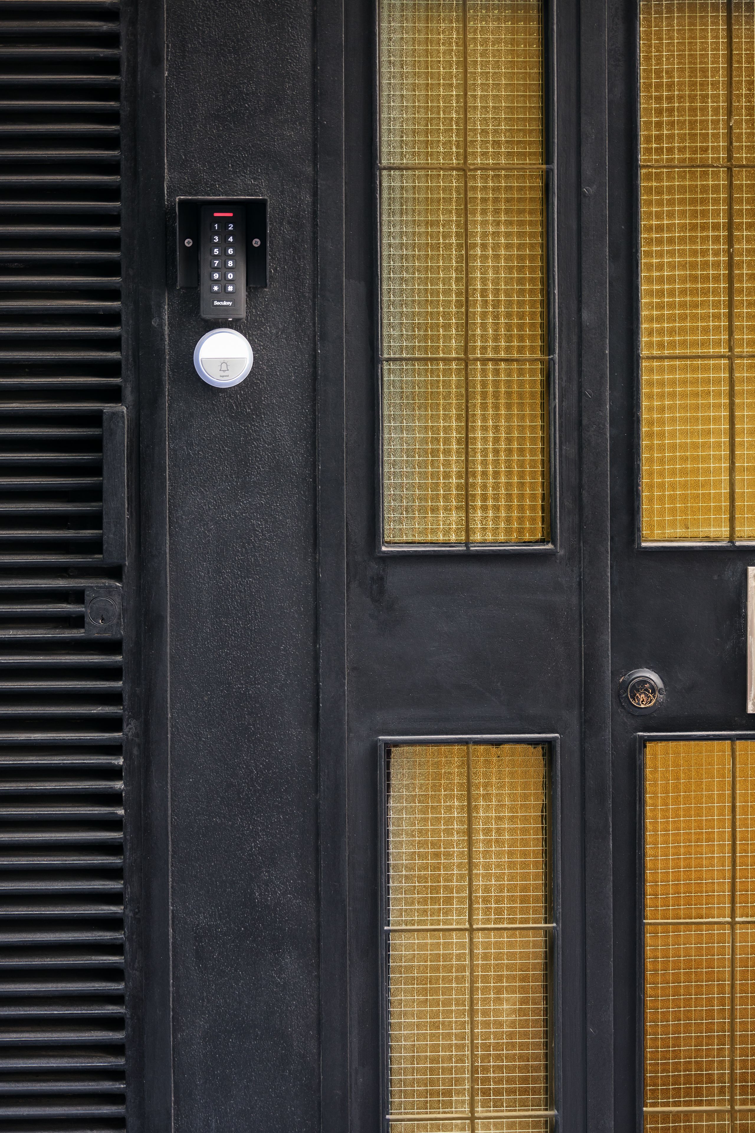 A black door with a keypad lock and a push-button alarm.