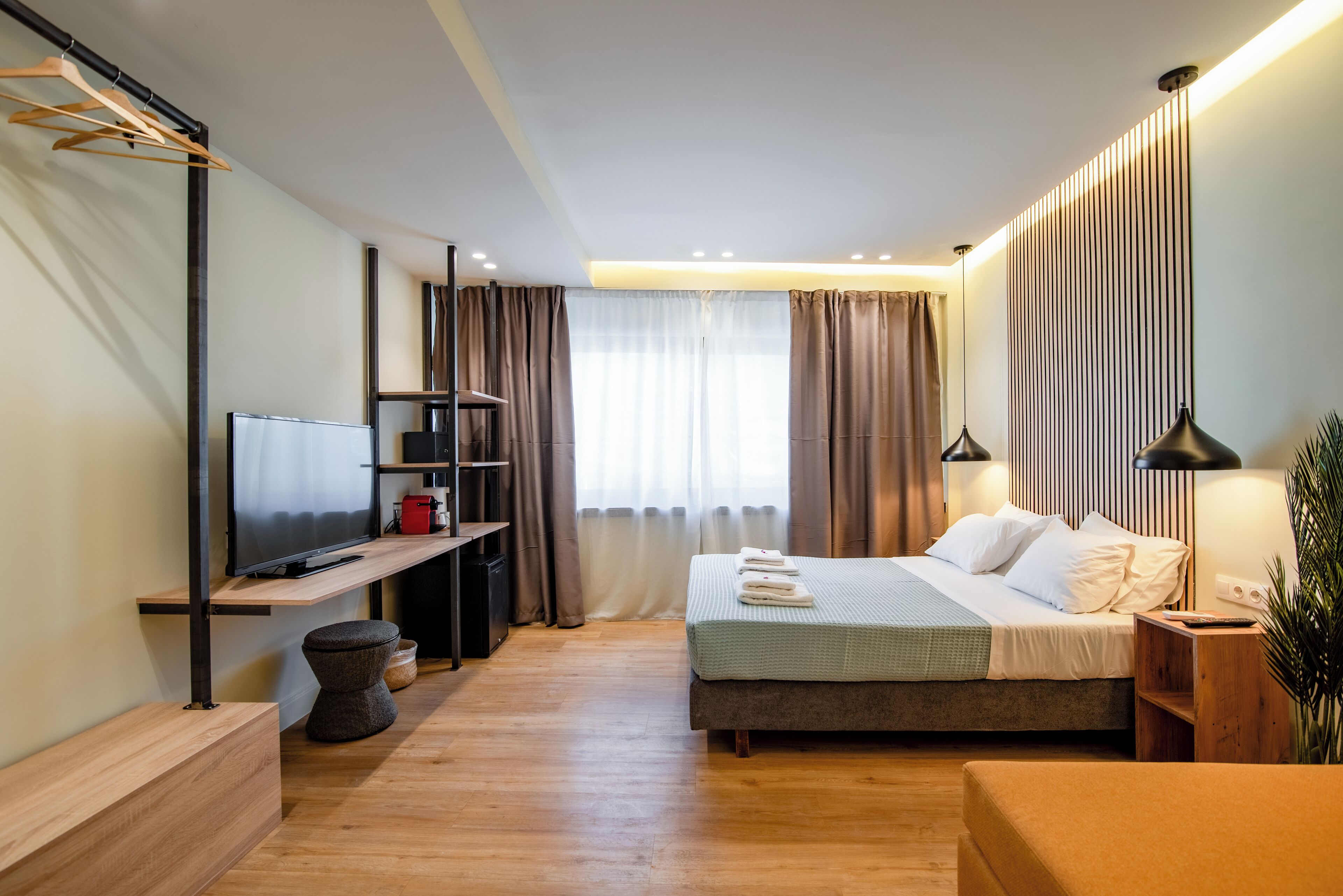 A modern hotel room with a bed, a TV, a desk, and a plant.