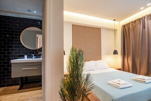 Camera d'albergo moderna con parete in mattoni scuri, uno specchio rotondo, un letto bianco con copriletto blu e pannello parete in listelli di legno.