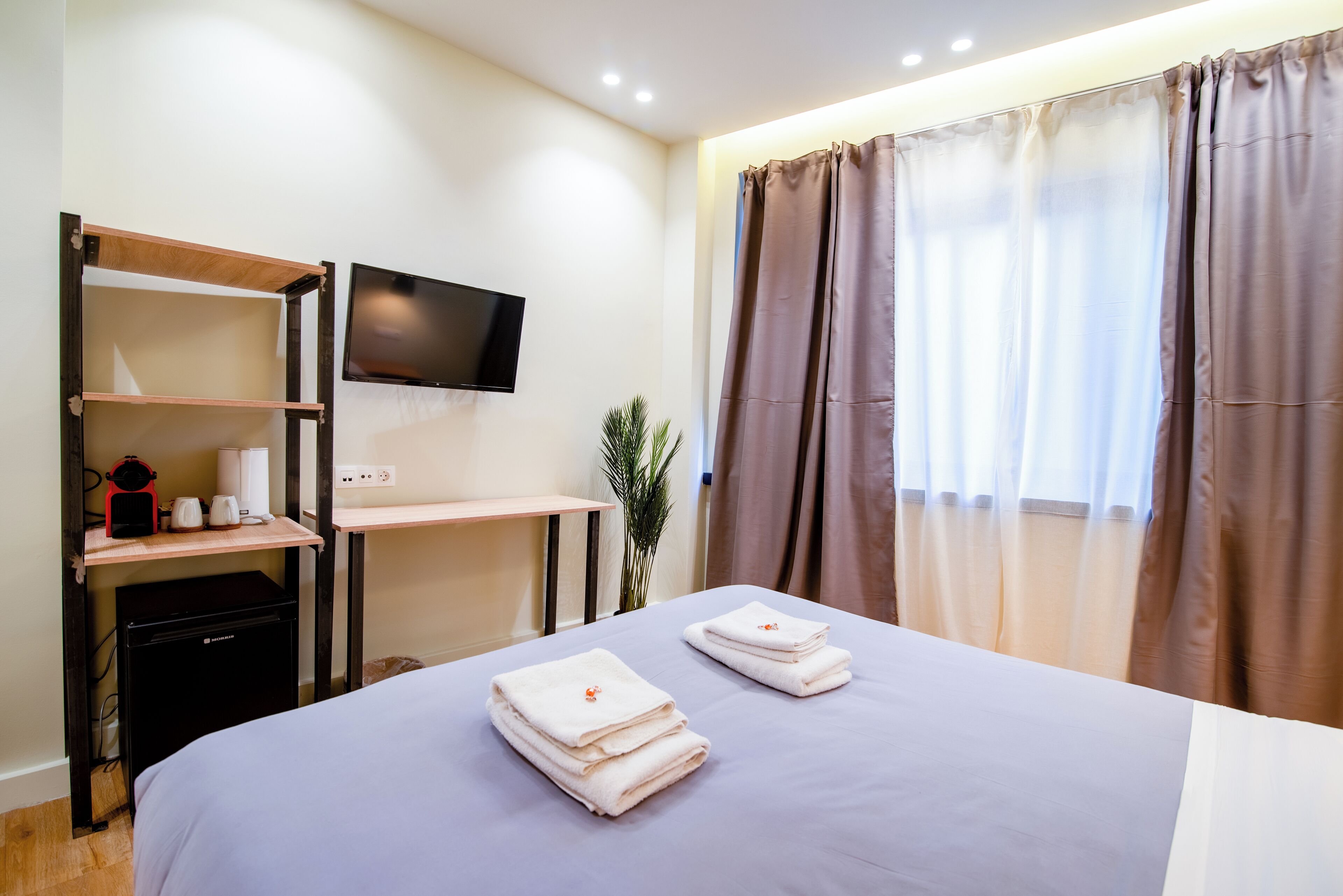 A hotel room with a bed, a desk, a TV, and a small kitchenette.