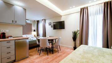 A modern kitchen with a dishwasher, a dining area with a round table and chairs, a bed with a headboard, and a TV mounted on the wall.