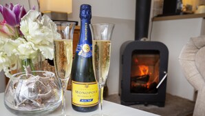 En champagneflaske og to glas på et bord, med en pejs i baggrunden.