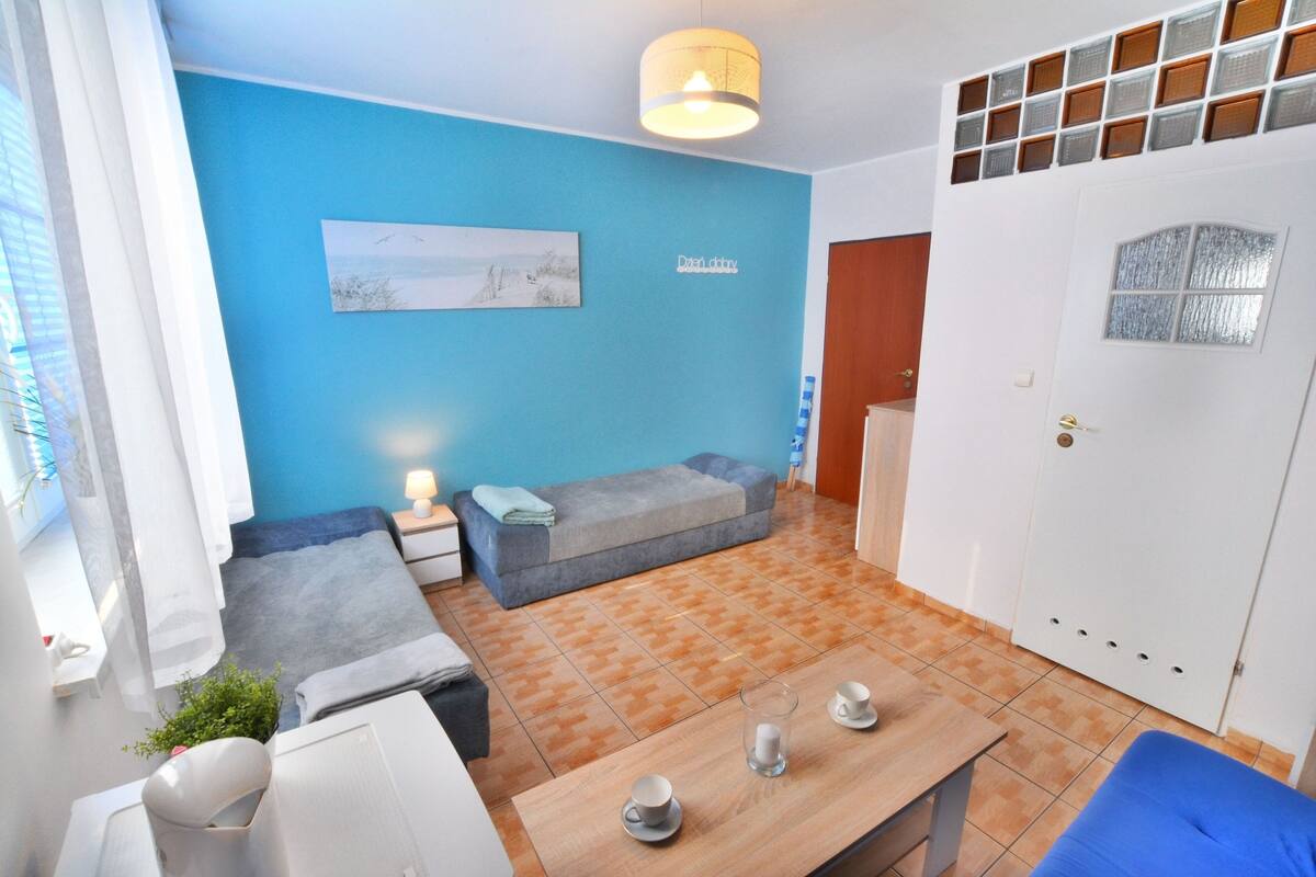 Ein Zimmer mit blauer Wand, einem grauen Sofa, einem Holztisch mit Tassen und einem weißen Kleiderschrank.