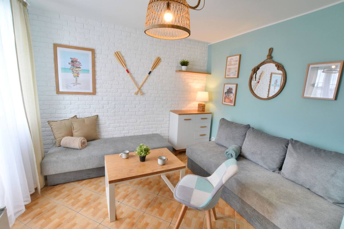 Ein modernes Wohnzimmer mit einer weißen Ziegelwand, zwei grauen Sofas, einem Holztisch und einem gemusterten Sessel.