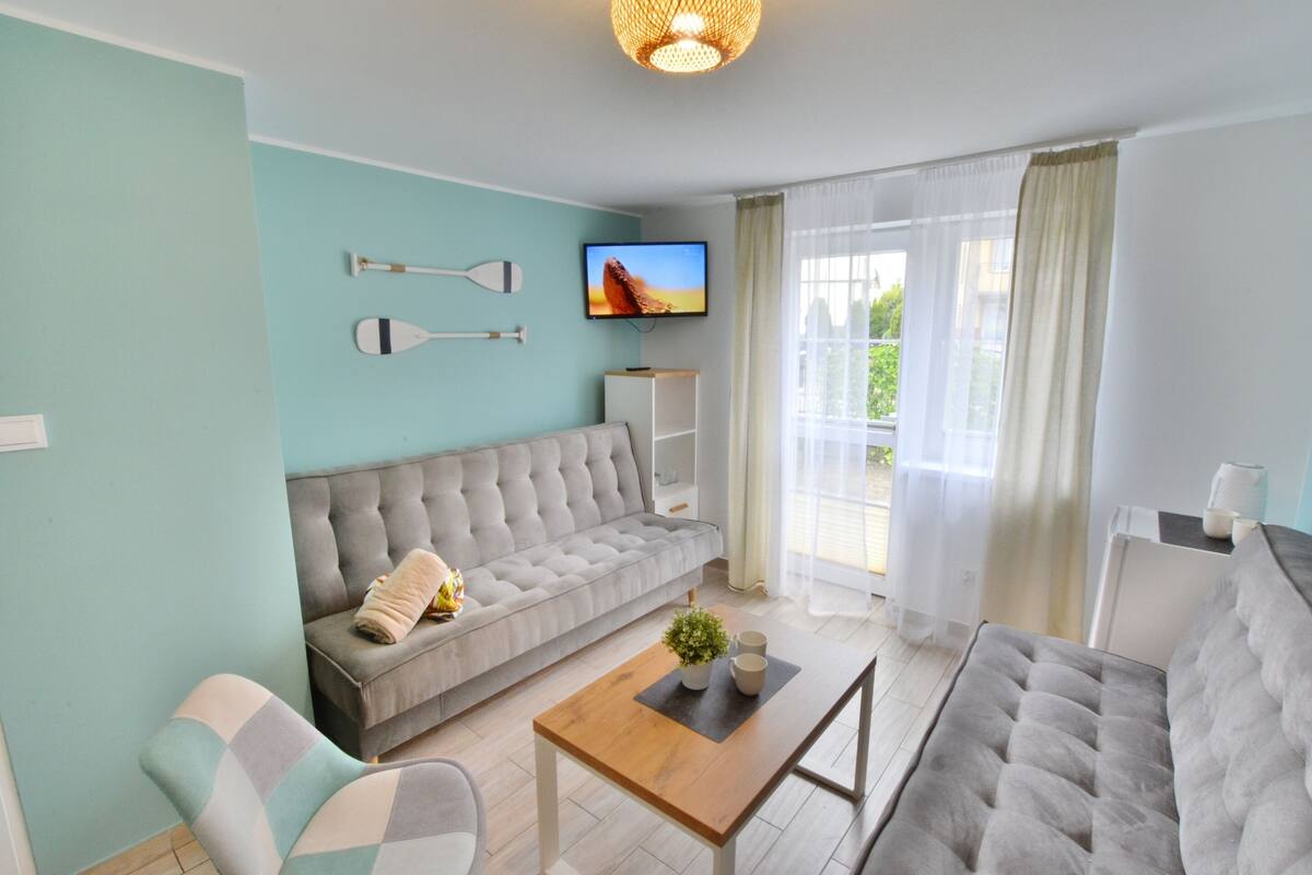 Ein modernes Wohnzimmer mit einem grauen Sofa, einem Holztisch und einem an der Wand befestigten Fernseher.