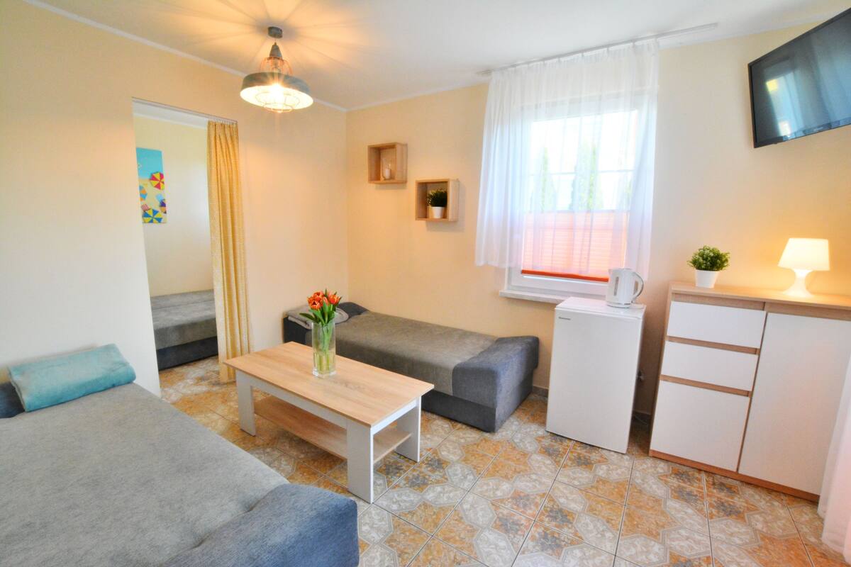 Ein gemütlicher, kompakter Wohnbereich mit einer Couch, einem kleinen Tisch, einer Küchenzeile und einem Fernseher.