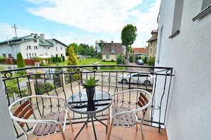 A balcony with a table and two chairs, overlooking a residential area with houses and a street.