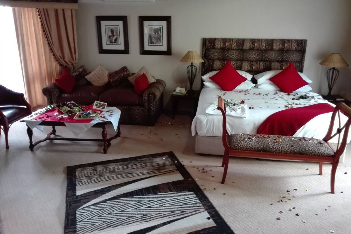 A hotel room with a bed, a sofa, a table with food, and a chair.