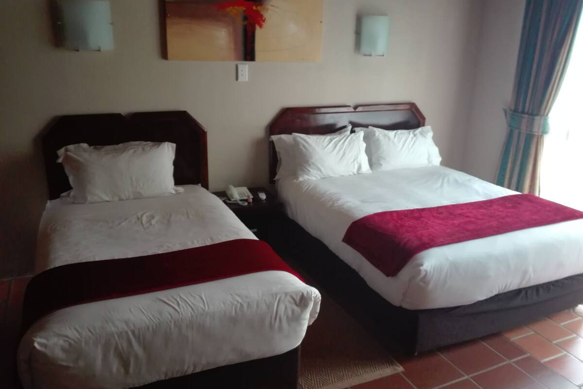 Two beds with white linens and red throw blankets, a telephone on the nightstand, and a wall-mounted artwork above the beds.