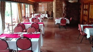 Un restaurant aux murs de briques, avec des poutres en bois au plafond, et des tables ornées de chaises rouges et de nappes blanches.