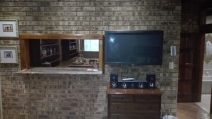 Un salon avec un mur en briques, un téléviseur à écran plat fixé au-dessus d’un meuble en bois et une cheminée.