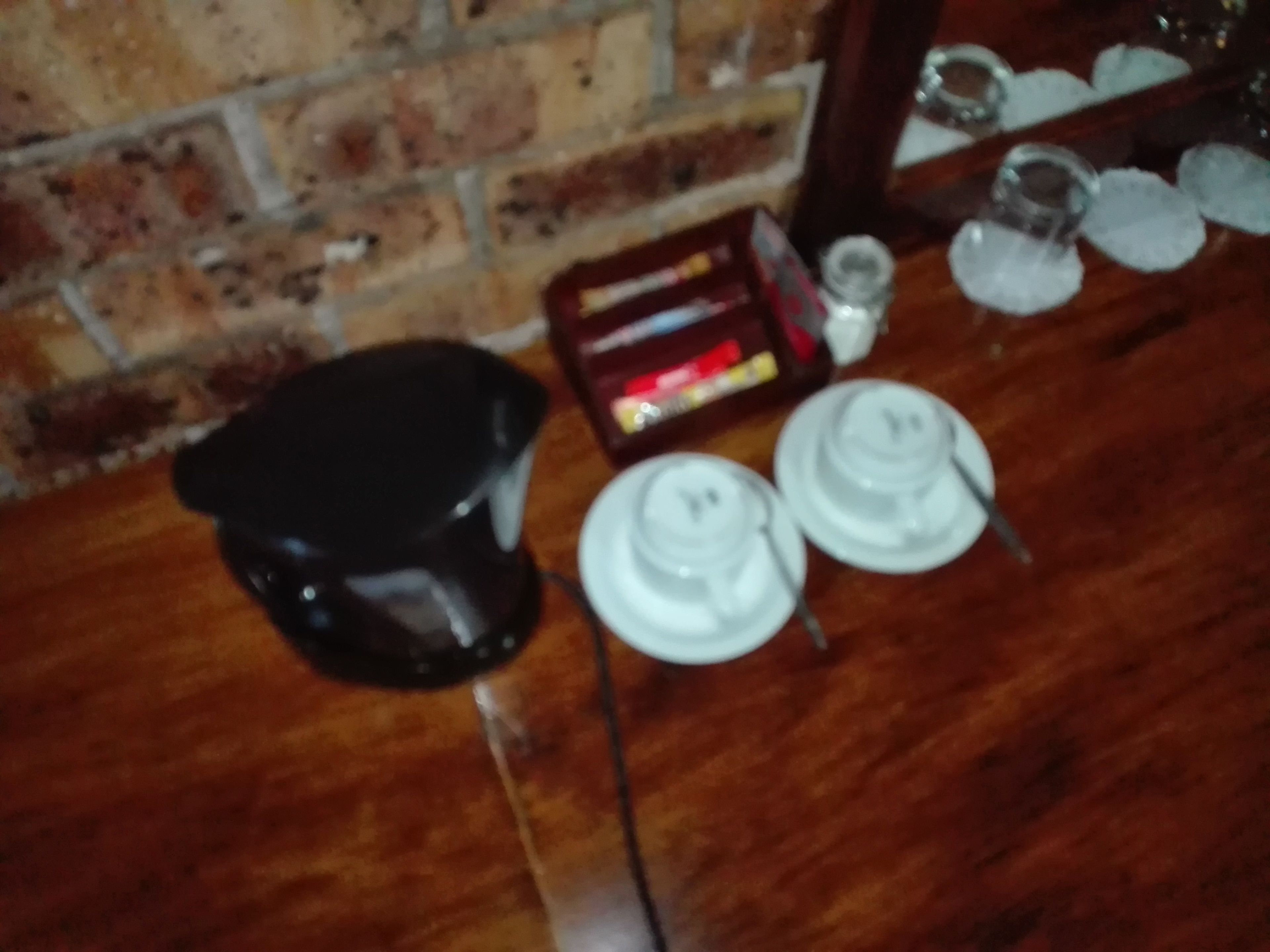 Una encimera de cocina con una cafetera, dos platos blancos, una caja roja y un frasco de vidrio.