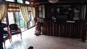 Un espace bar chaleureux, avec des meubles en bois, un sol en briques et une vue dégagée grâce à de grandes fenêtres ornées de rideaux à motifs.