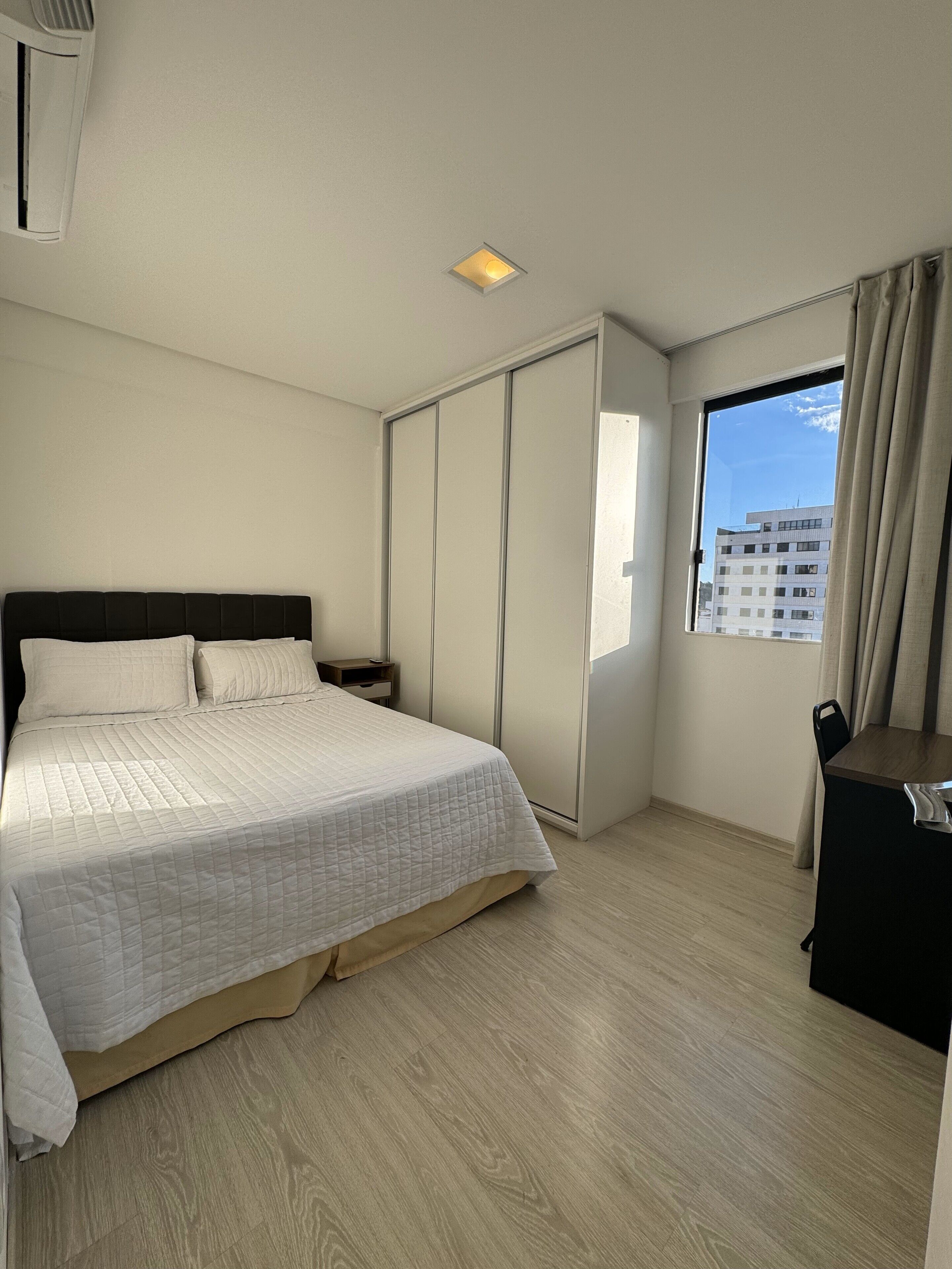 A bedroom with a bed, a wardrobe, a desk, and a window with curtains.