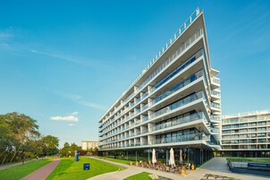 A modern hotel with multiple floors, outdoor seating area, and a parking lot.