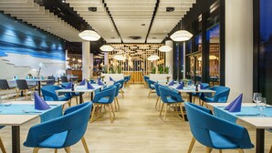 A modern restaurant interior with blue chairs, wooden tables, and a central decorative wall. - Seaside Park Hotel (Kolobrzeg)