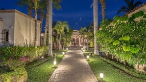 A pathway leading to a building surrounded by palm trees and well-maintained gardens. - Cabocasabuenavista- WALK TO Private Beach. Roof top deck.  Pets welcome (San Jose Del Cabo)