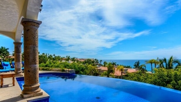 An infinity pool with a clear view of the ocean and palm trees in the background. - Cabocasabuenavista- WALK TO Private Beach. Roof top deck.  Pets welcome (San Jose Del Cabo)