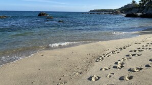 A sandy beach with footprints leading to the water, a rocky shoreline, and a clear blue sky. - Cabocasabuenavista- WALK TO Private Beach. Roof top deck.  Pets welcome (San Jose Del Cabo)