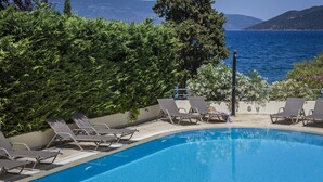 A pool with lounge chairs and a view of the sea and mountains. - Meliti Waterfront Suites (Kefalonia)