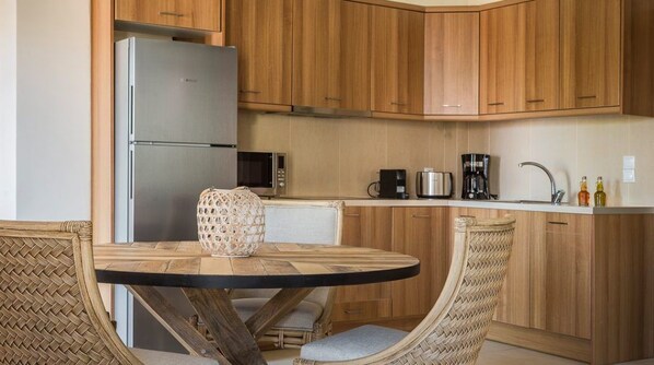 Una cocina compacta con armarios de madera, un refrigerador de acero inoxidable, un microondas, una cafetera y una mesa redonda con sillas de mimbre.