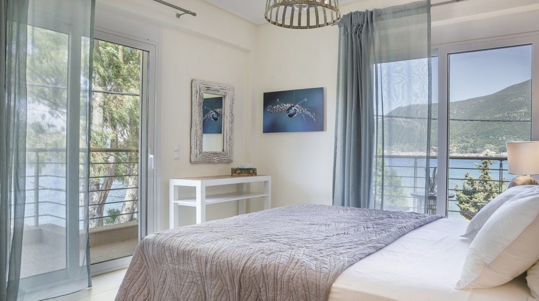 A bedroom with a bed, a bedside table, a mirror, and a view of the sea.