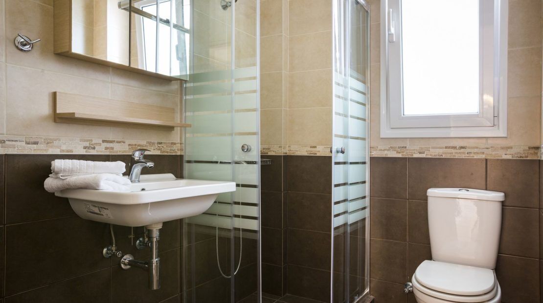 A bathroom with a glass shower enclosure, a white sink, and a toilet.