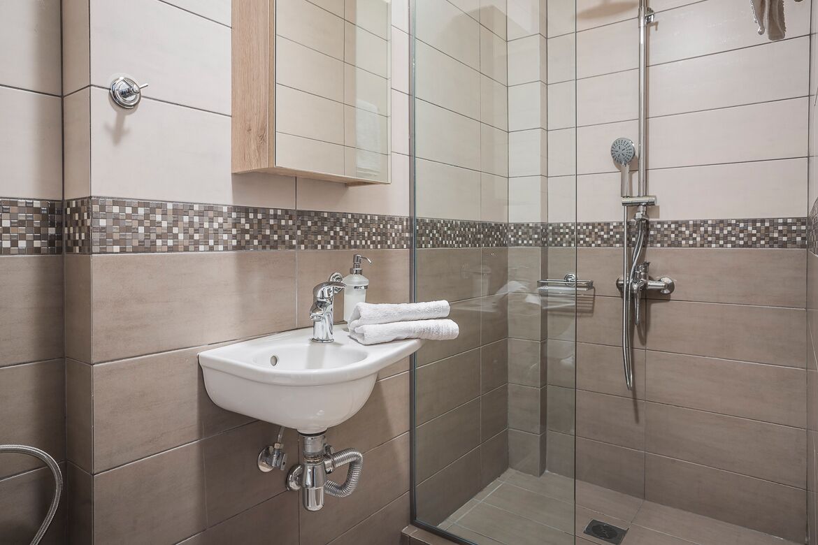 A modern bathroom with a glass shower enclosure, a sink with a mirror, and a tiled backsplash.