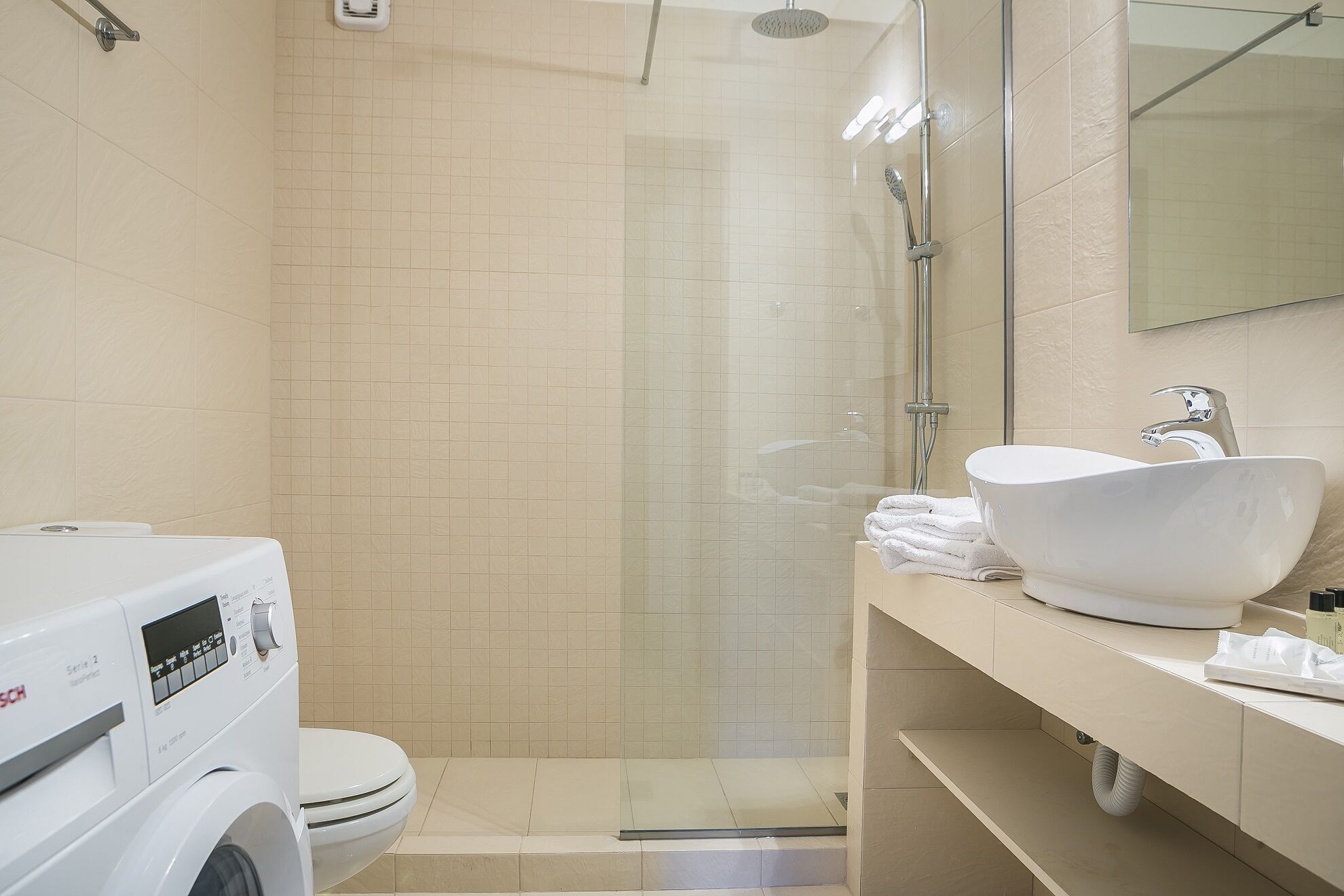 Une salle de bain moderne avec une douche à parois de verre, un lavabo blanc et un lave-linge.